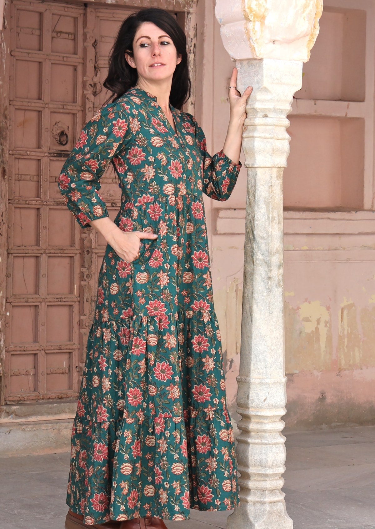 Model standing sideways with hands in pocket wearing a dark green cotton dress in floral print.