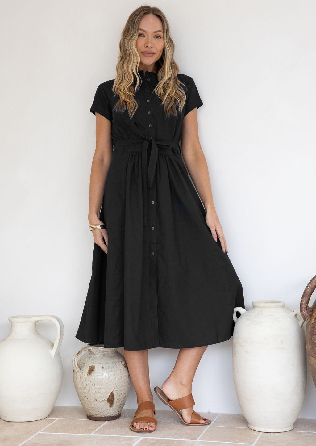 Woman wearing a midi length button through 50's style black cotton dress with a waist tie