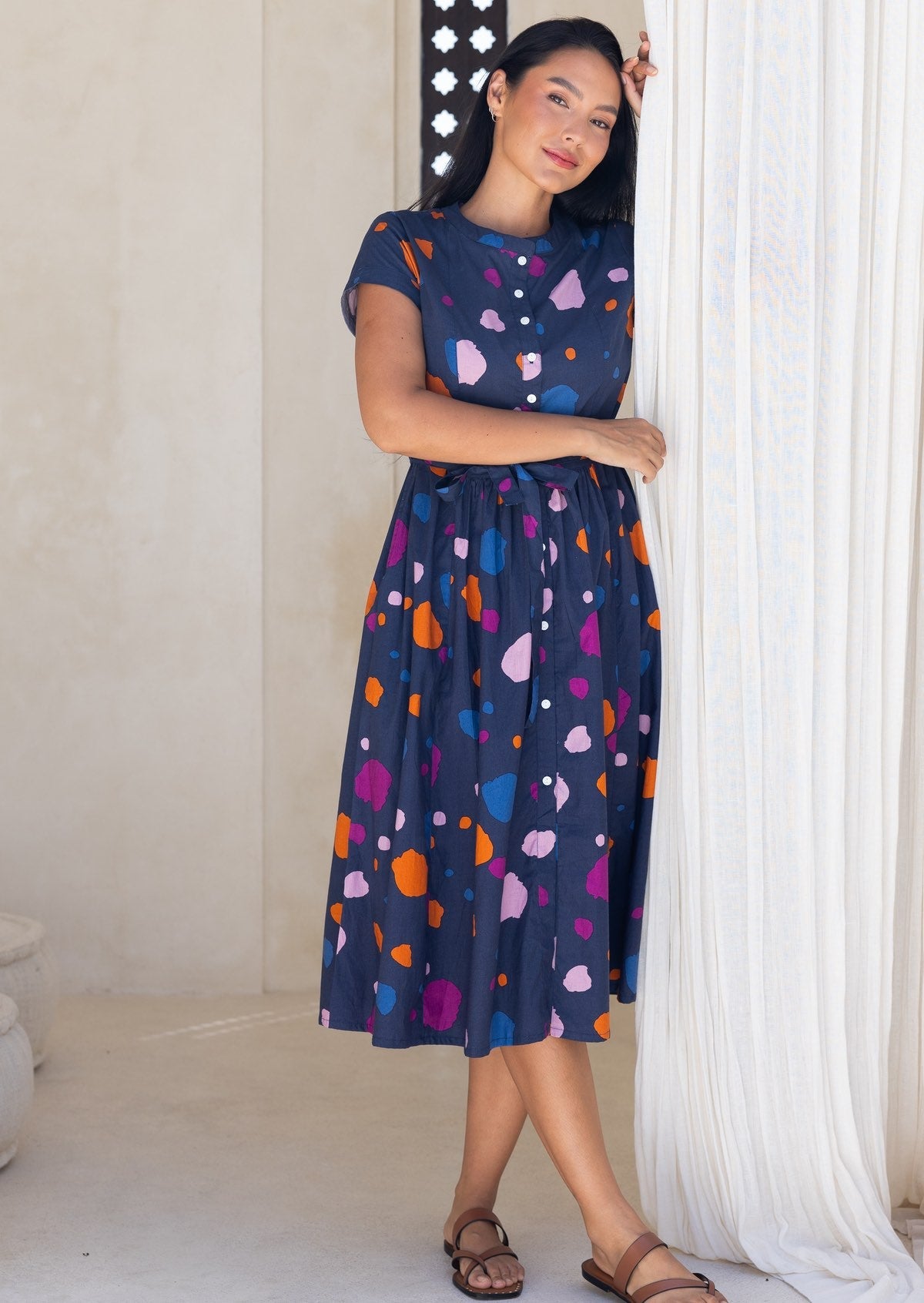 Woman wearing a navy based cotton 50's style button through midi length dress with colourful polka dot print