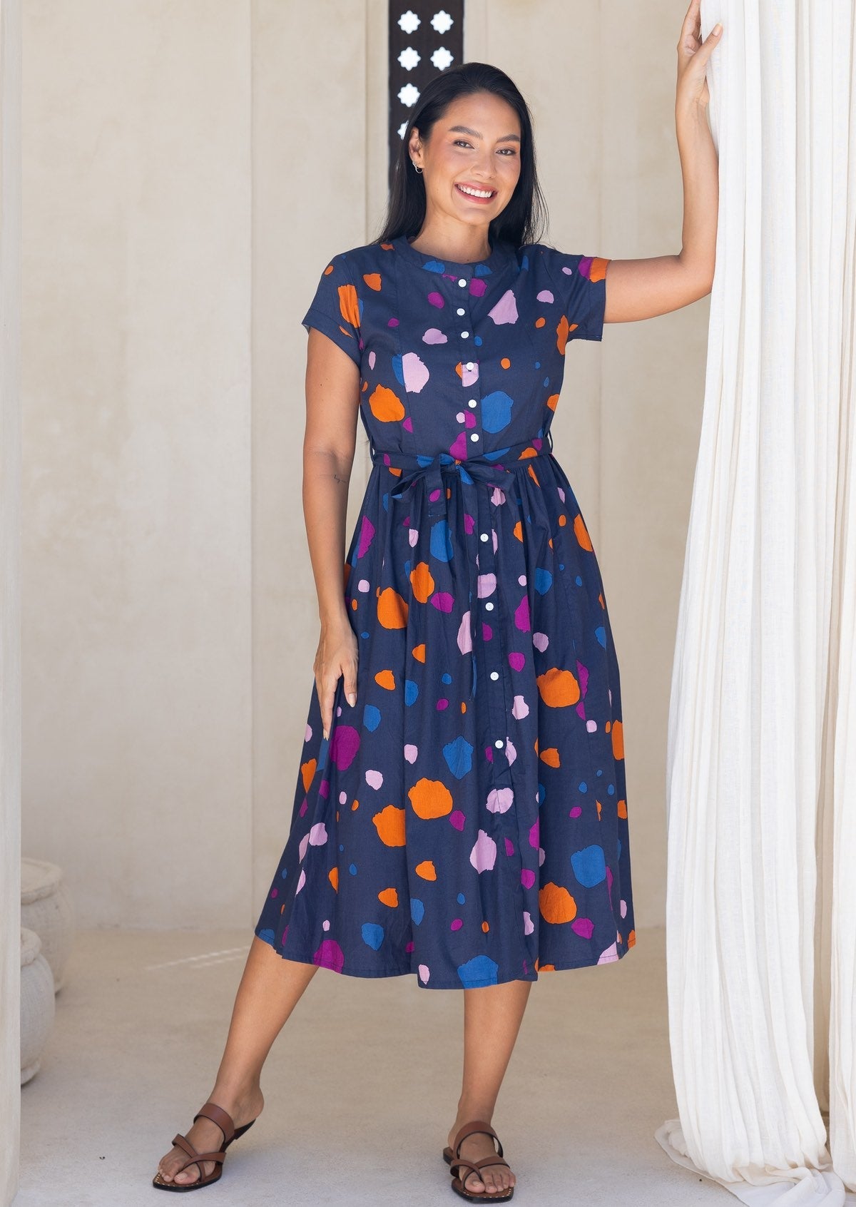Woman wearing a navy based cotton 50's style dress with colourful polka dot print