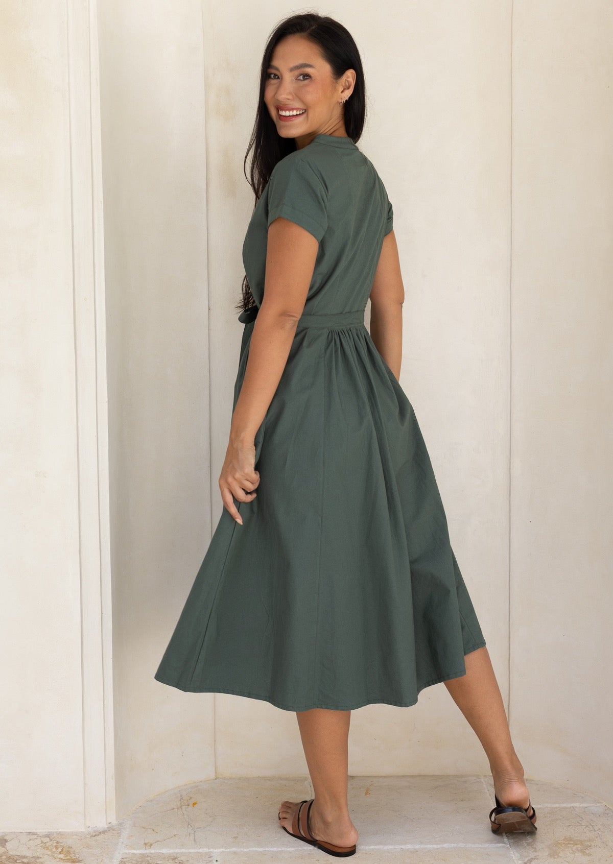 Back view of a woman wearing a 50's style moss green cotton dress with small gathers at the back of the waist