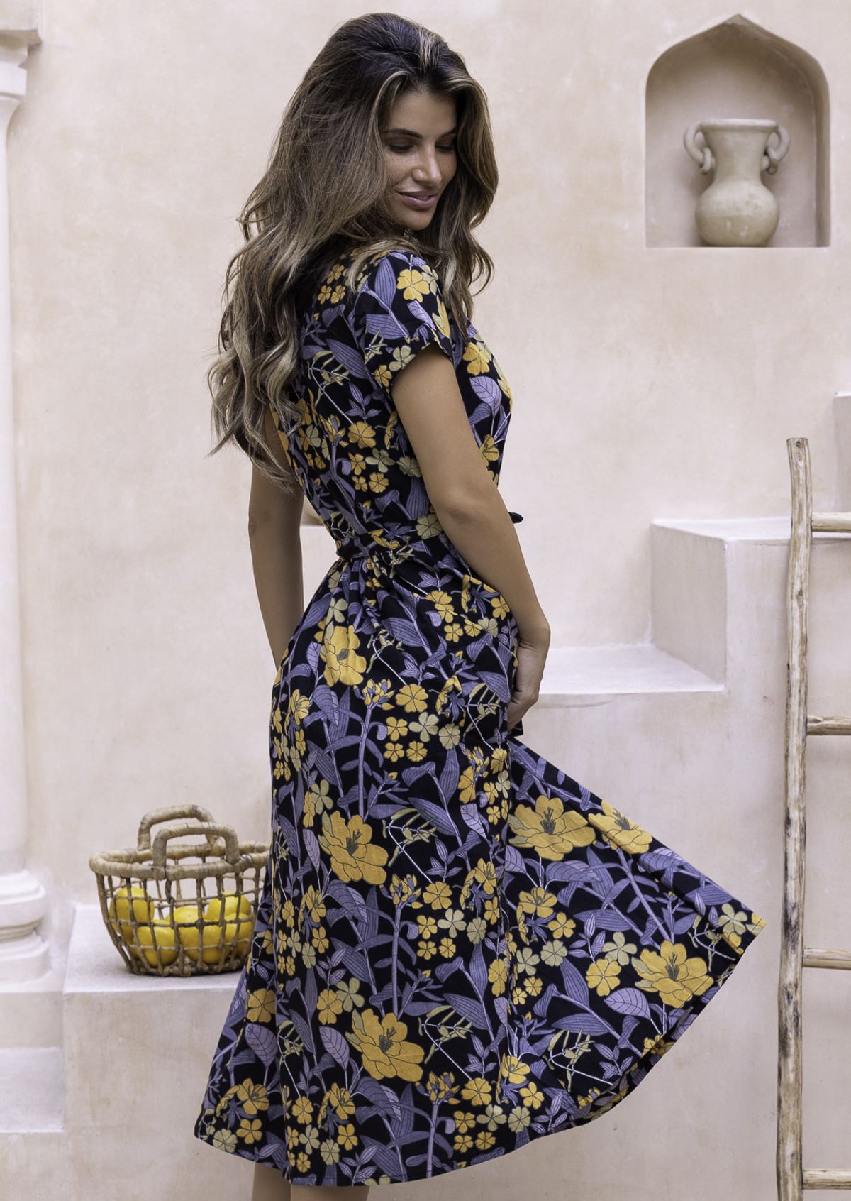 Side pose of model wearing a yellow, green, grey floral cotton dress with detachable waist tie, short sleeves and high mandarin collar.