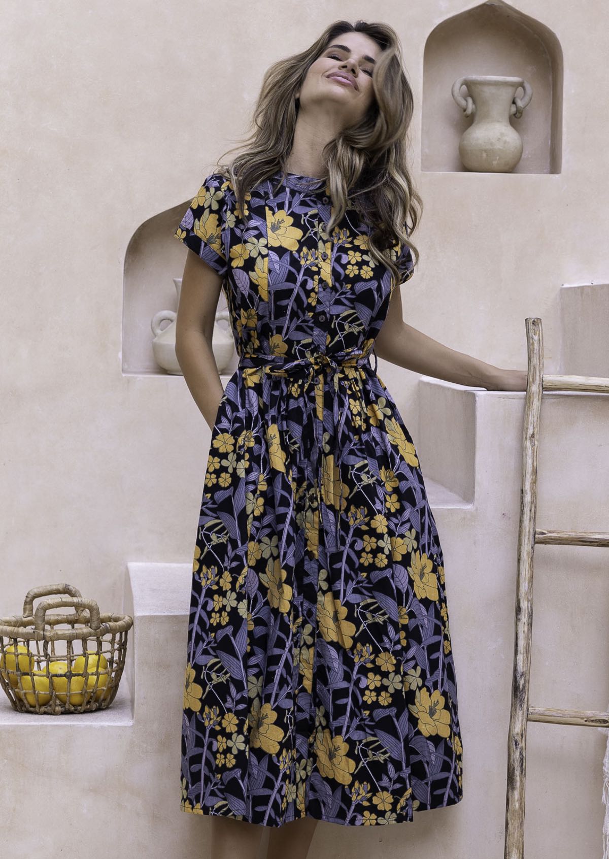 Woman wearing a floral 1950's inspired cotton dress with mandarin collar that can folded to form V neckline, short sleeves and pockets.