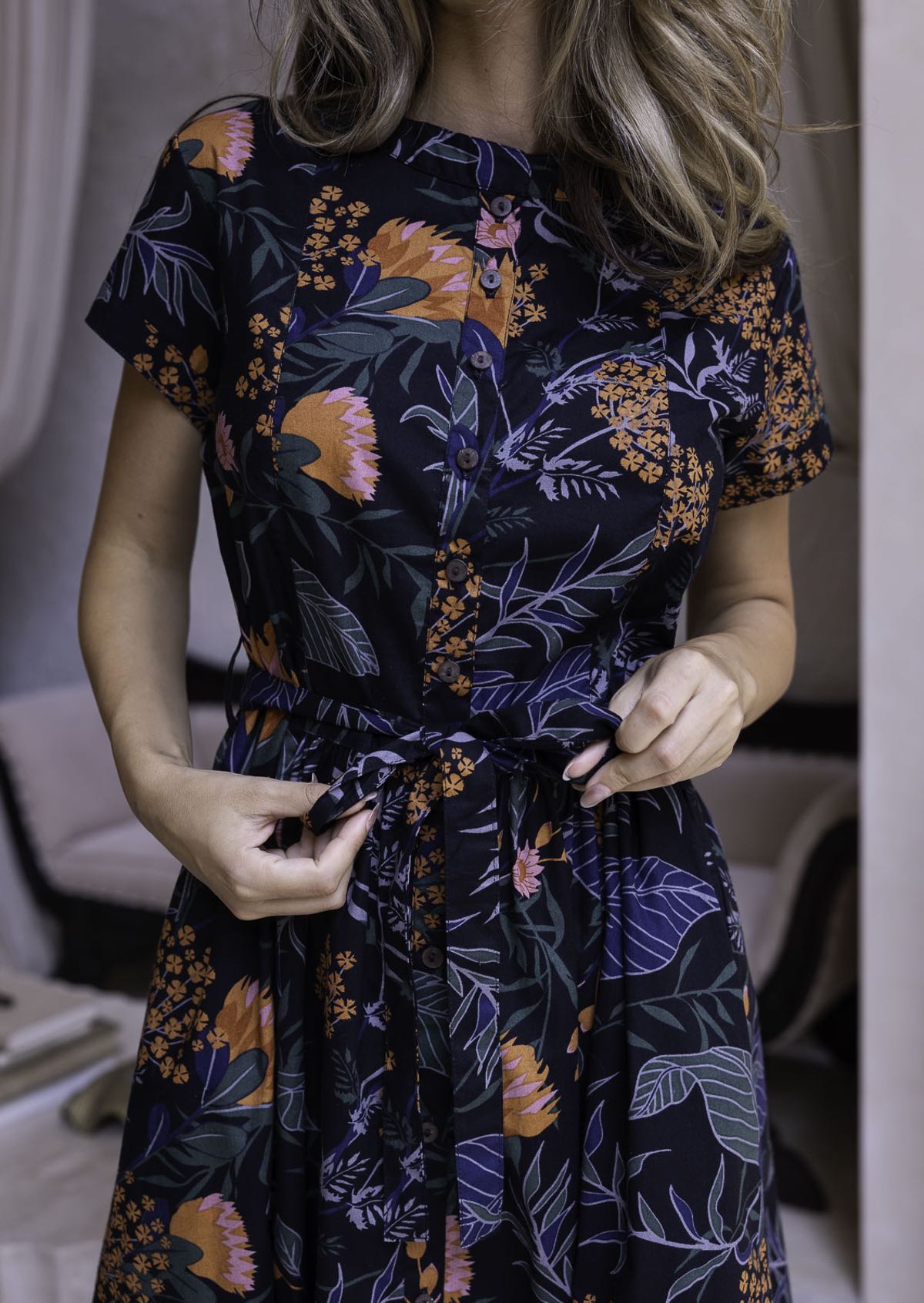 Model holds the fabric waist tie on a 1950's inspired beautiful botanical print dress with buttons in the centre front.