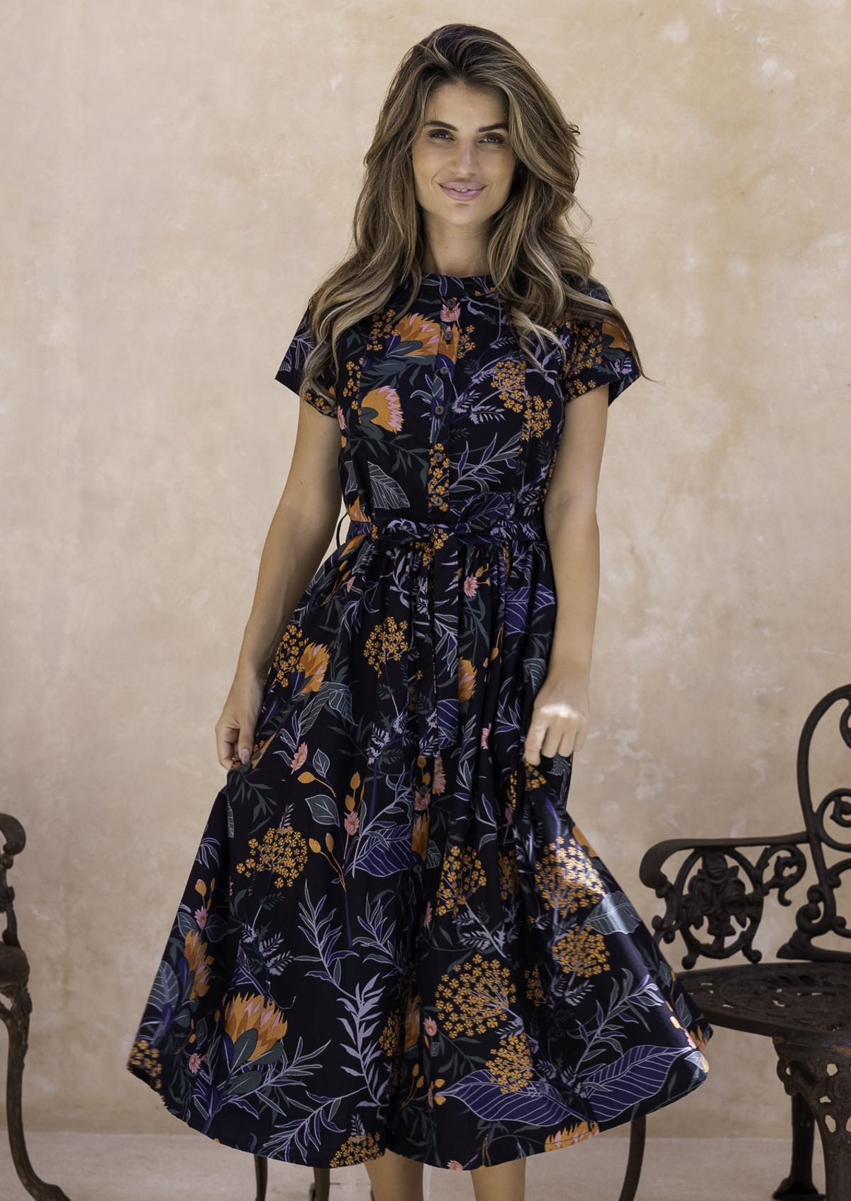 Model flaunting a retro style botanical print dress with detachable waist tie, pleats at the waist and hidden side pockets.