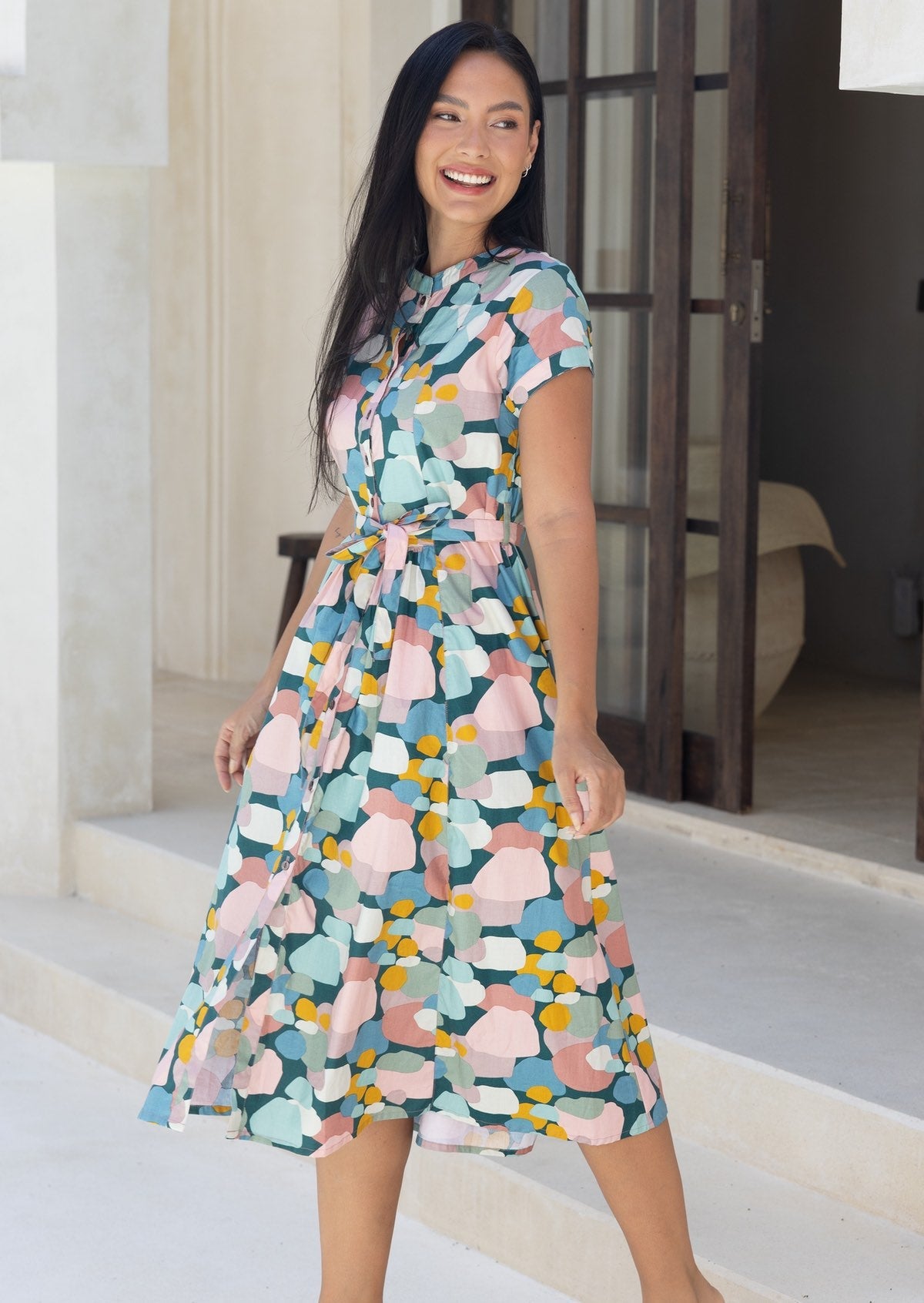 Woman standing in cotton 50's style button through dress in pastel colours with cap sleeves and waist tie