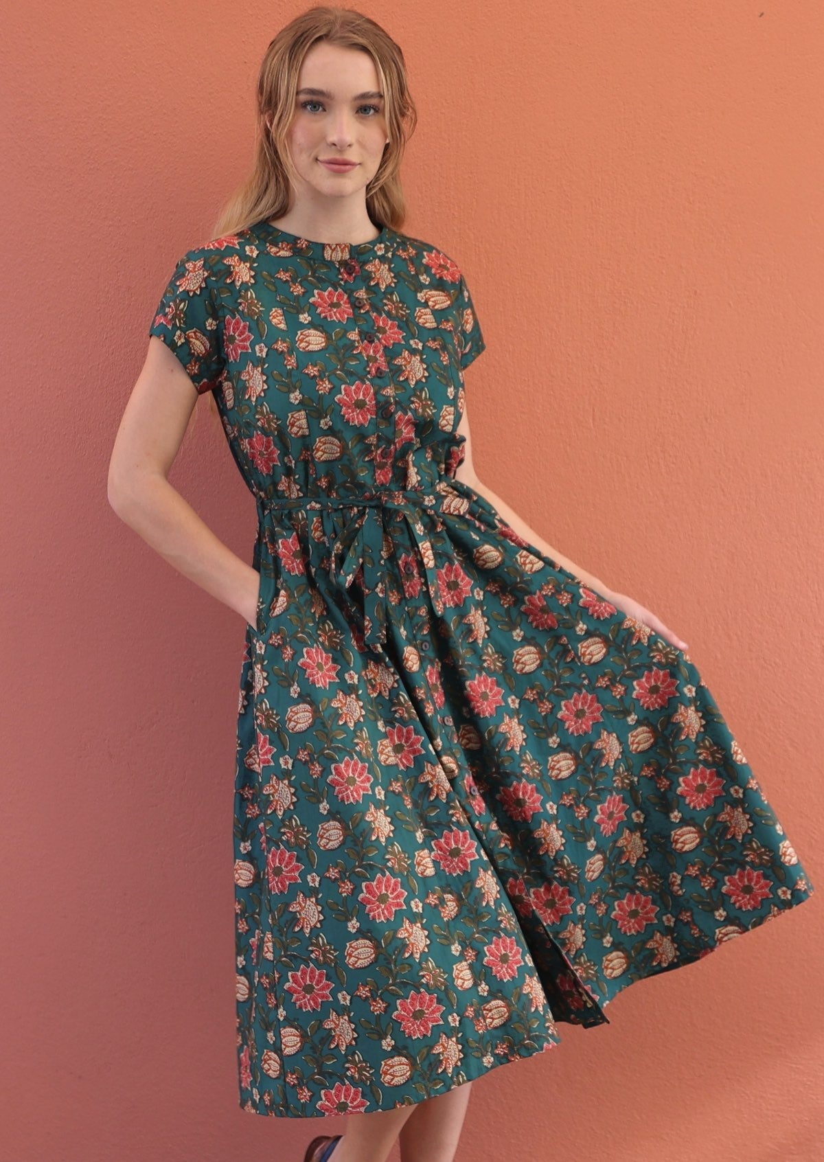 Model standing in green cotton dress with short sleeves and pockets.