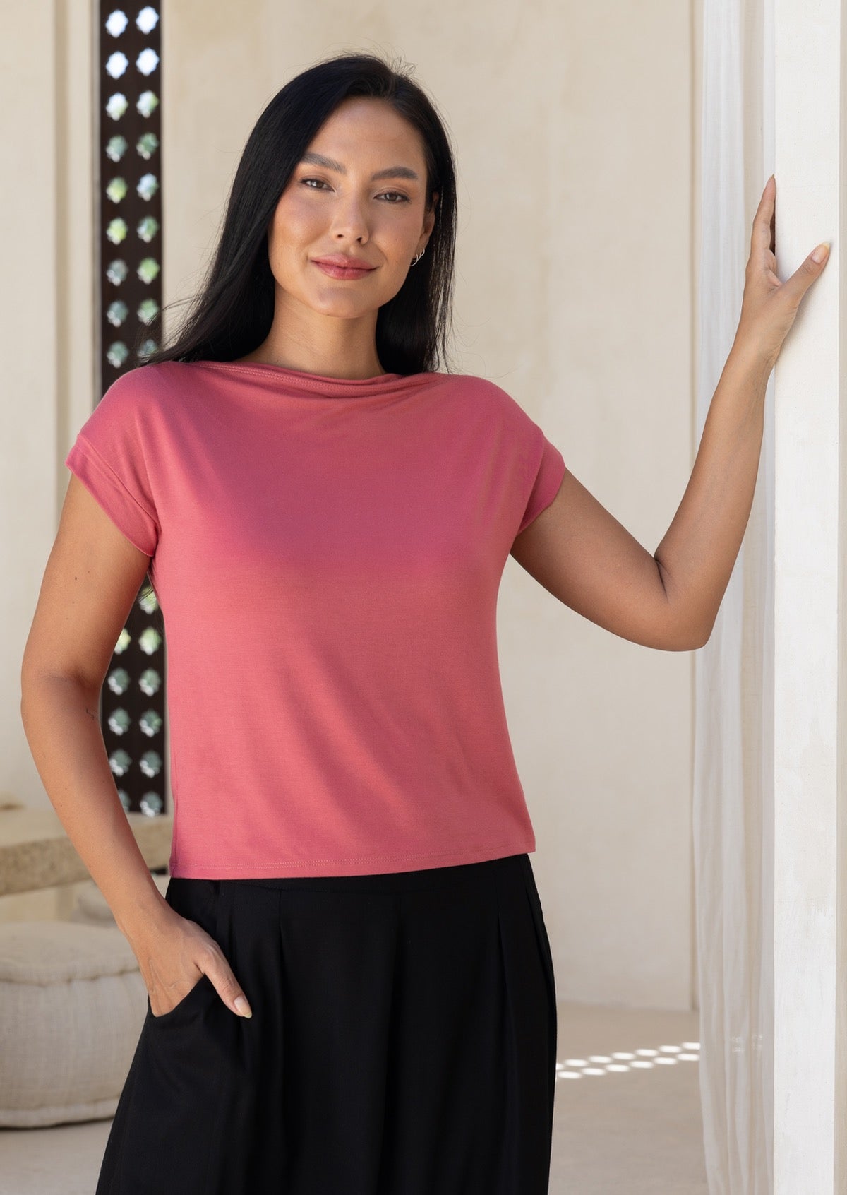 Woman wearing a pink stretch rayon t-shirt with a wide neckline and black pants