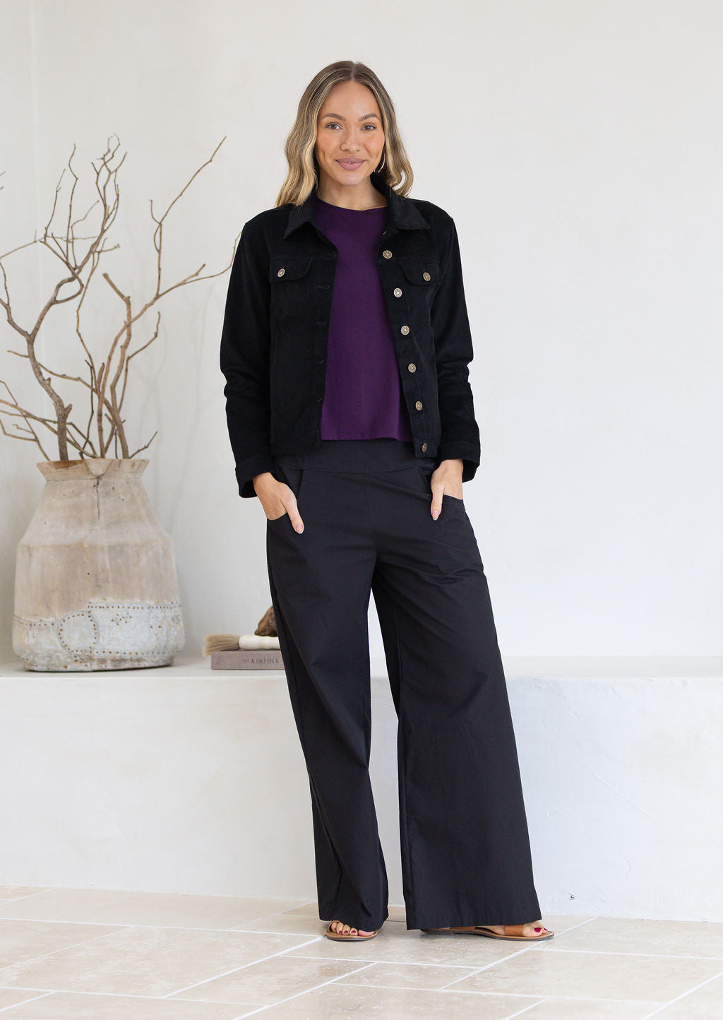 Woman wearing a black corduroy jacket and pants with a purple shirt indoors.