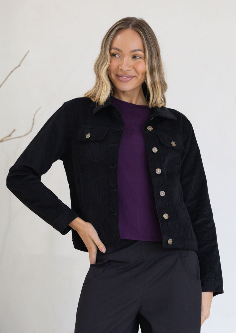 Woman wearing a black corduroy jacket over a purple shirt with a white background