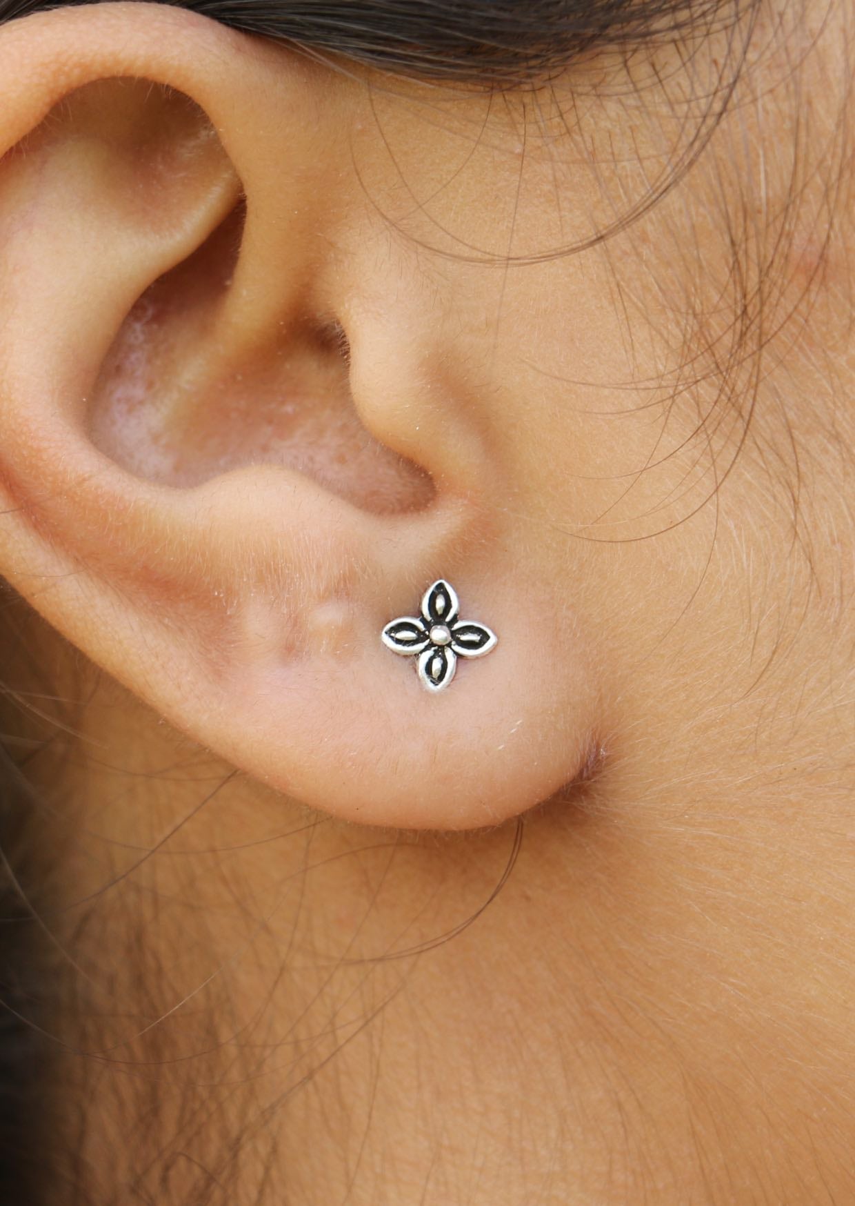 Close-up of an ear wearing a Zieria Silver Studs with a delicate four-petal leaf design