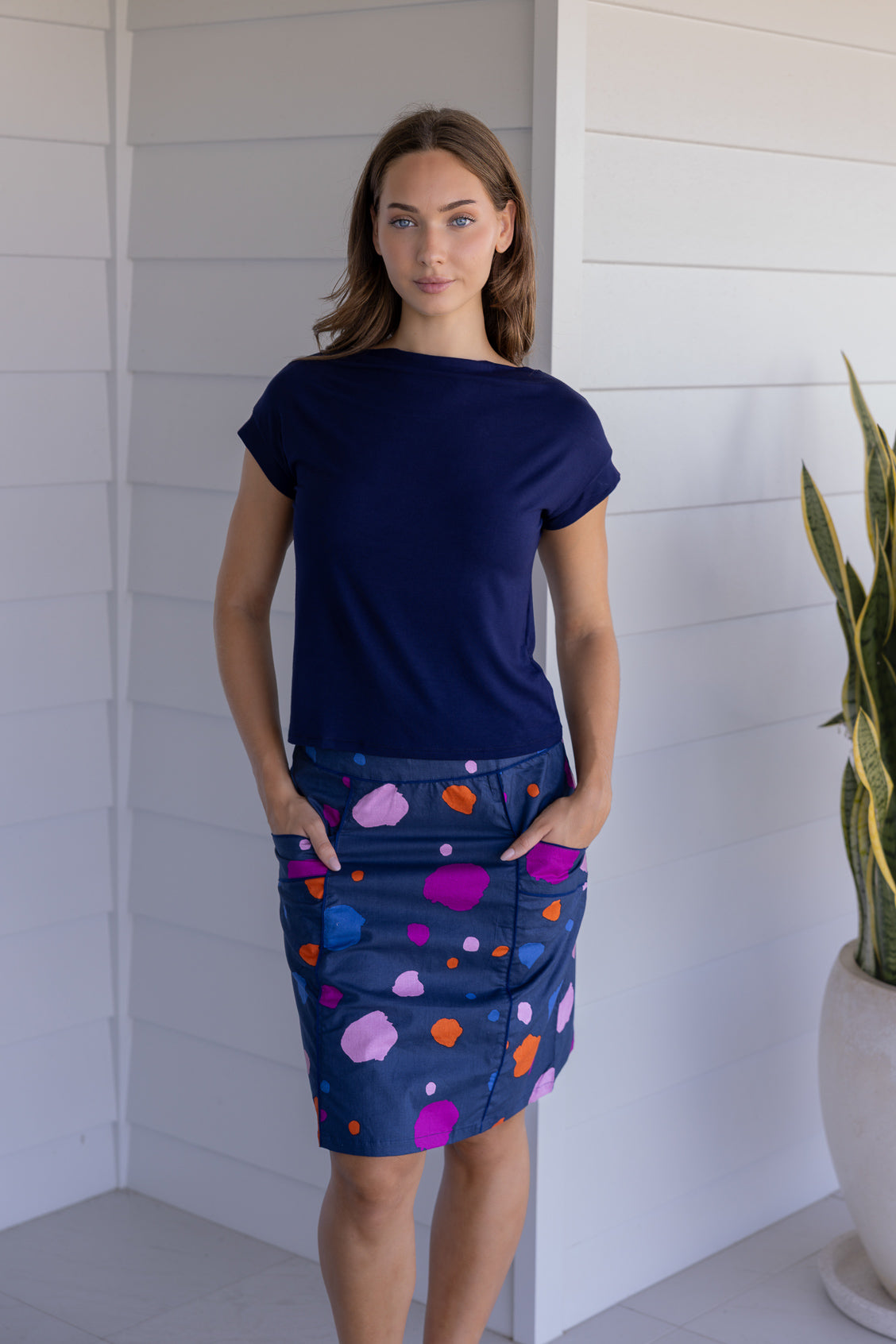Woman wearing a knee length skirt with blue, orange, plum and pale pink splotch print, paired with a basic top