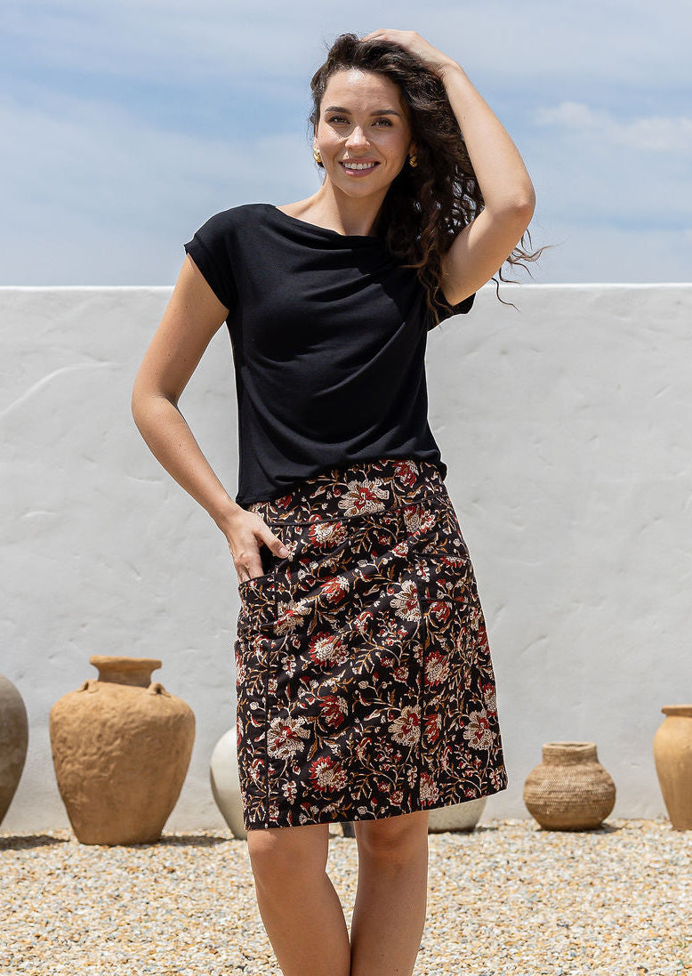 Woman in a black top and cotton dark floral skirt standing outdoors with pottery in the background