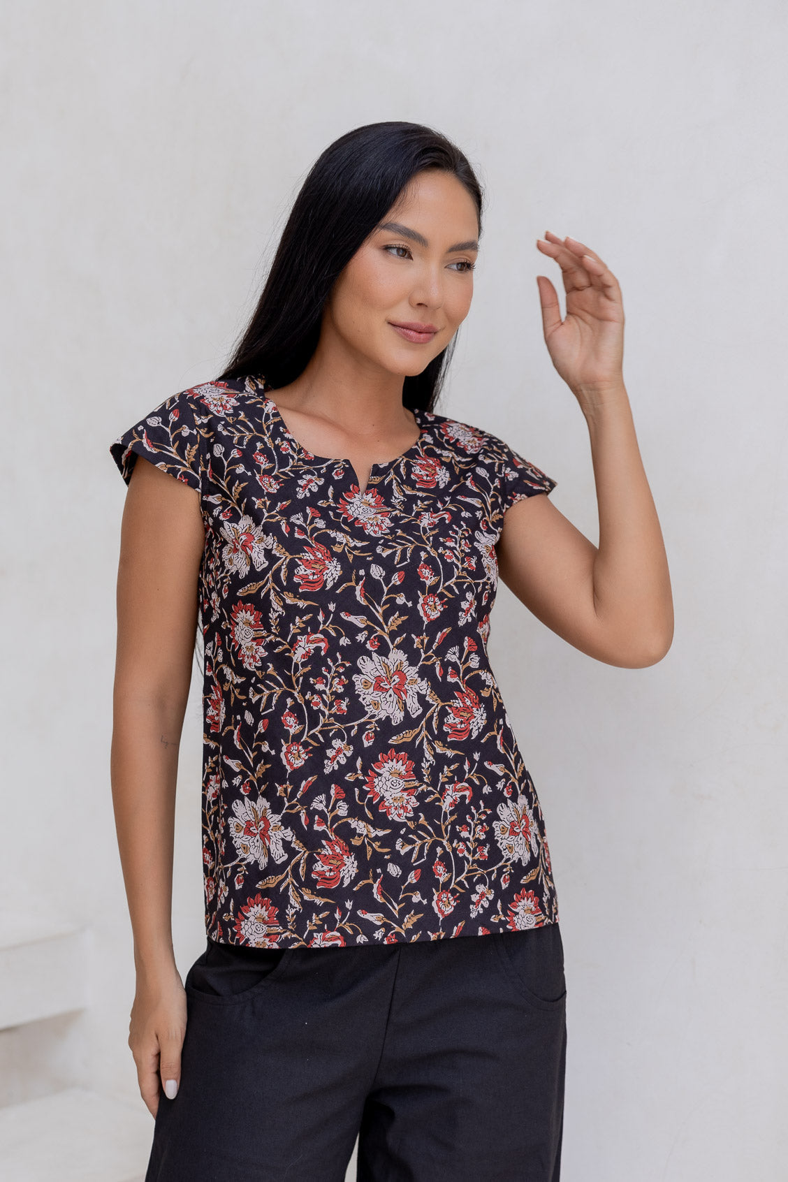 Model wears cotton cap sleeved tailored top in indian traditional floral print on a dark base.