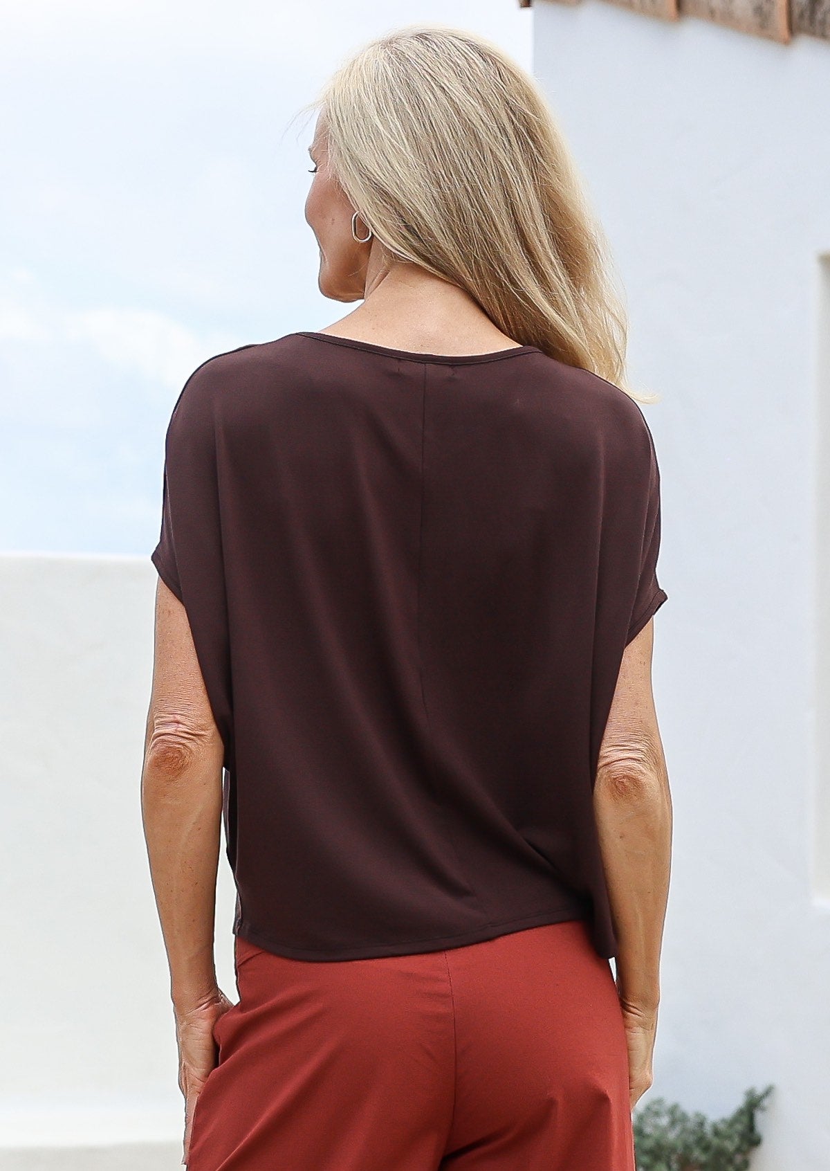 woman wearing a brown top and burnt henna pants against a light background