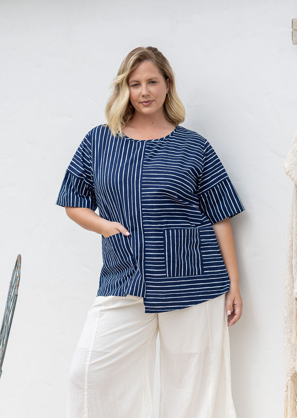 Woman wears a navy and white striped 100% cotton relaxed fit top with an asymmetrical hem line.