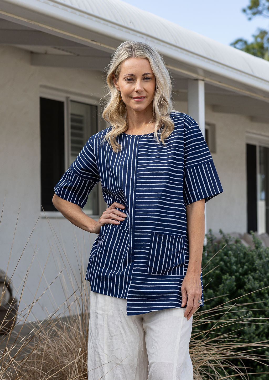 Woman wears a navy and white striped 100% cotton relaxed fit top with short sleeves and front pockets