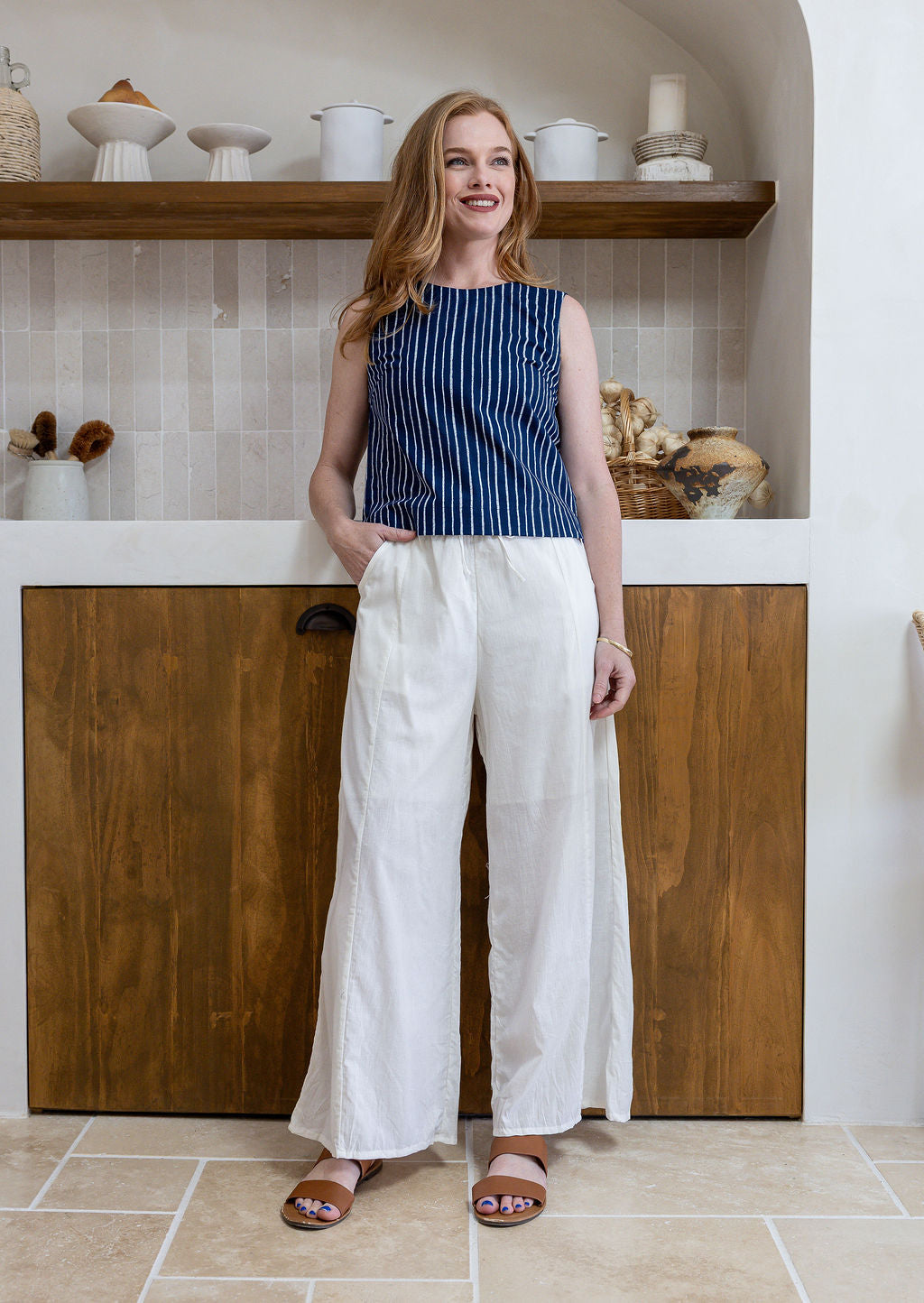 Model stands in white plain pants and relaxed fit floral print top with round neckline, sleeveless design and side bust darts.