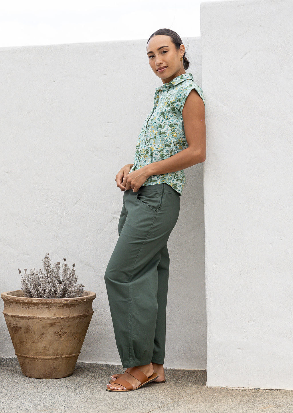 Woman standing sideways wearing a floral printed slim fit cotton shirt with plain green pants.