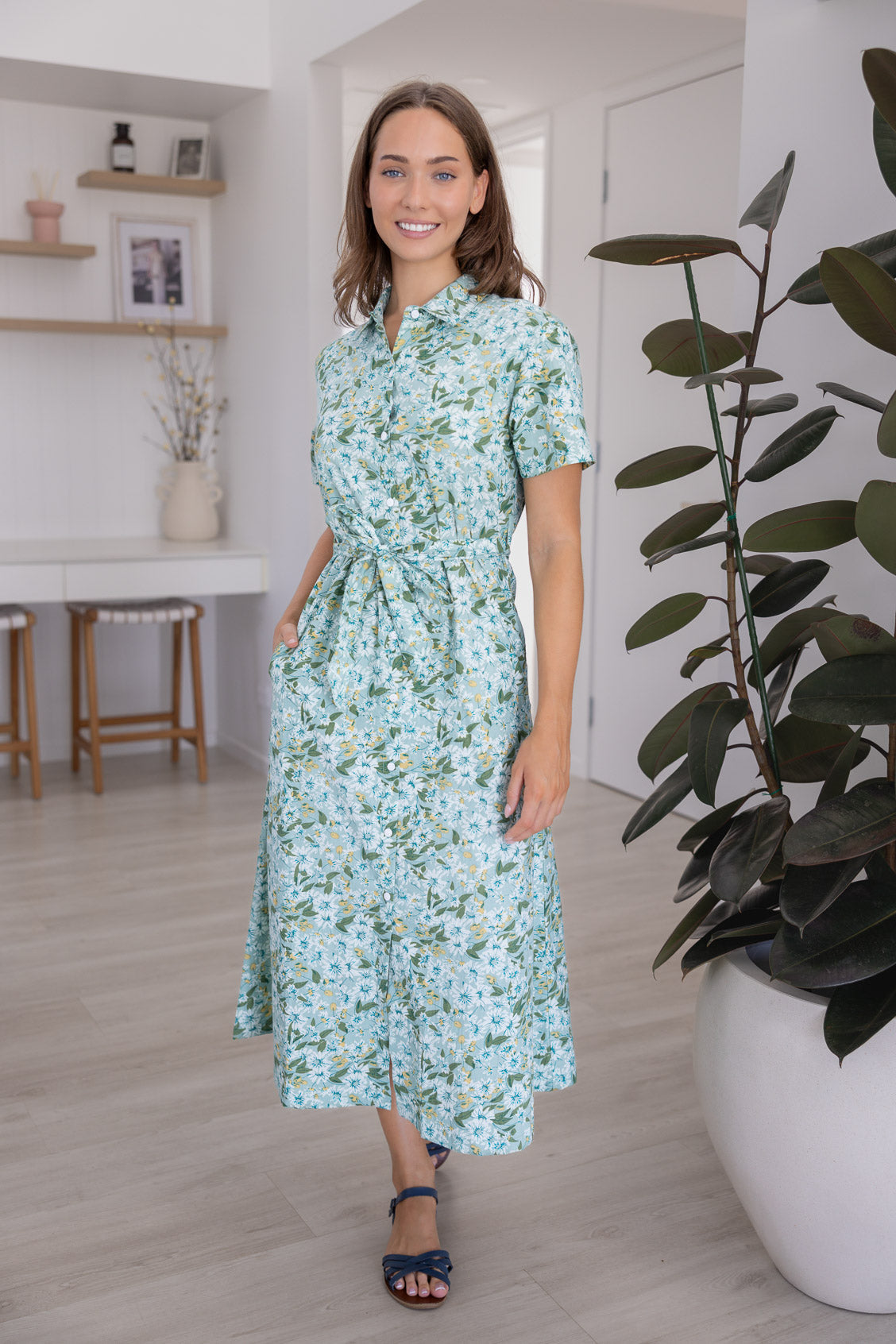 Woman wearing 100 percent cotton button through shirt dress with collar and short sleeves, in a sage green based floral print.