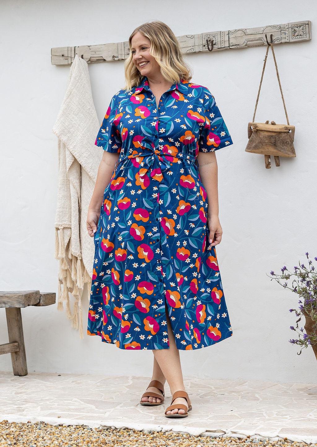 Woman wearing 100 percent cotton button through shirt dress with collar and short sleeves, in a royal blue based floral print.