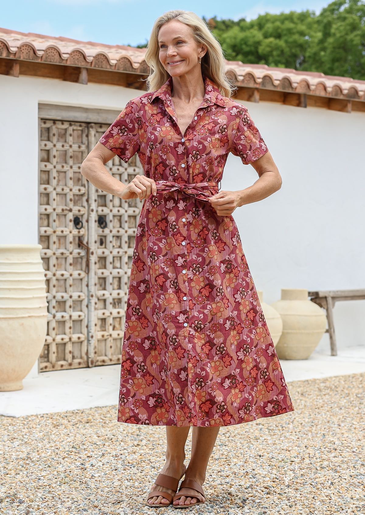 Woman wearing a midi length shirt style cotton dress with short sleeves, button through front and a detachable fabric waist tie in japanese style warm floral print.
