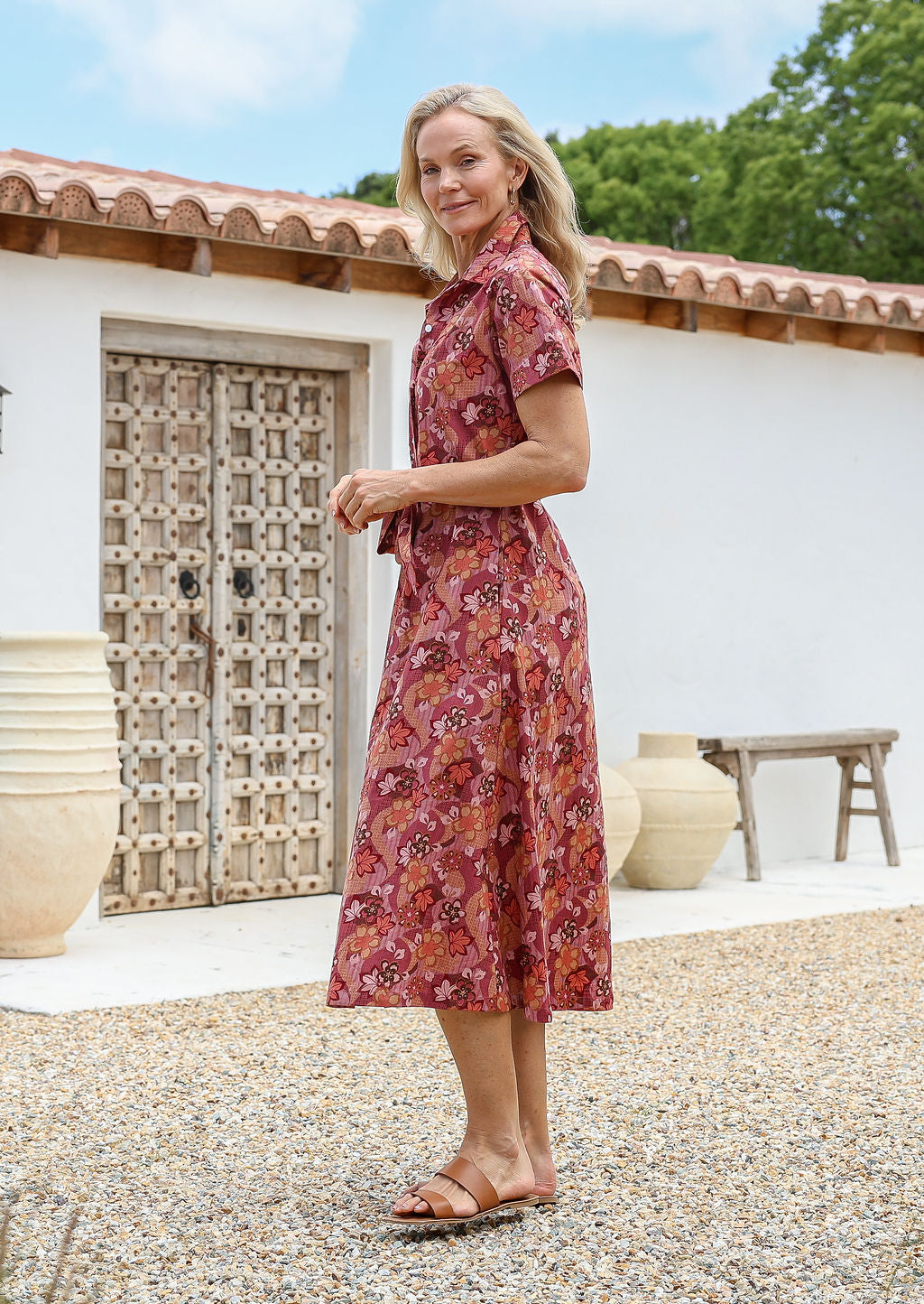 Woman standing in a midi length 1950s style shirt dress with structured collar, short sleeves, waist tie and pockets.