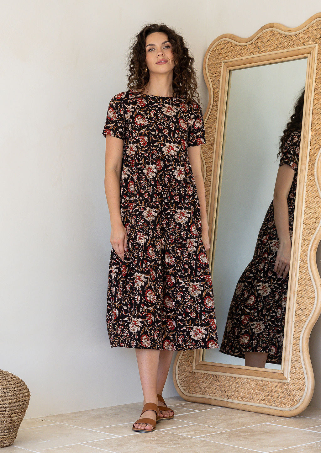 Woman wearing a black based floral cotton midi length dress with tiered skirt and short sleeves