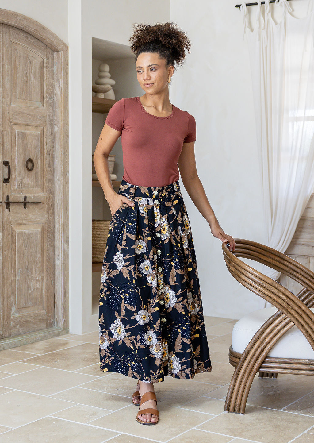 Woman standing with a hand in pocket in a minimalistic room wears 100% cotton button through skirt in black based floral print.