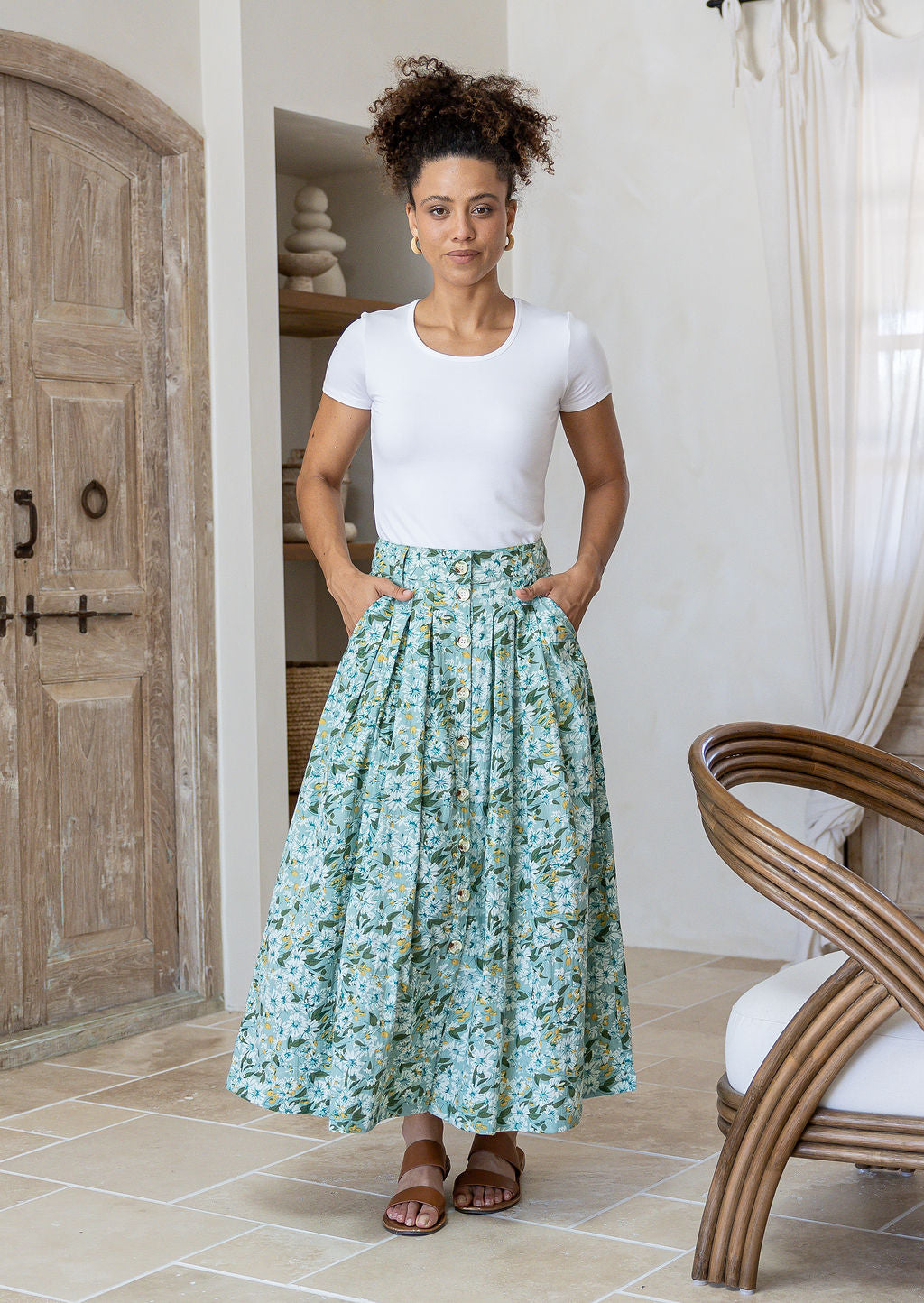 Woman wearing a white basic top and floral button through shin length cotton skirt with box pleats, belt loops and pockets.