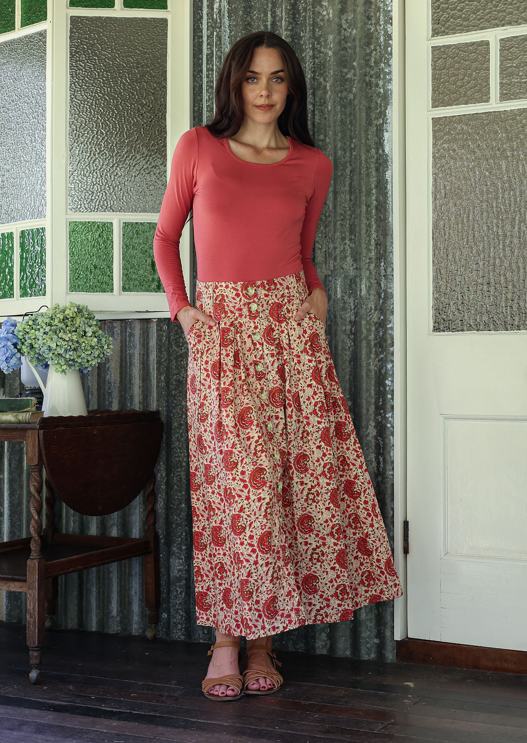 Woman wearing a pink top and floral skirt standing in a room