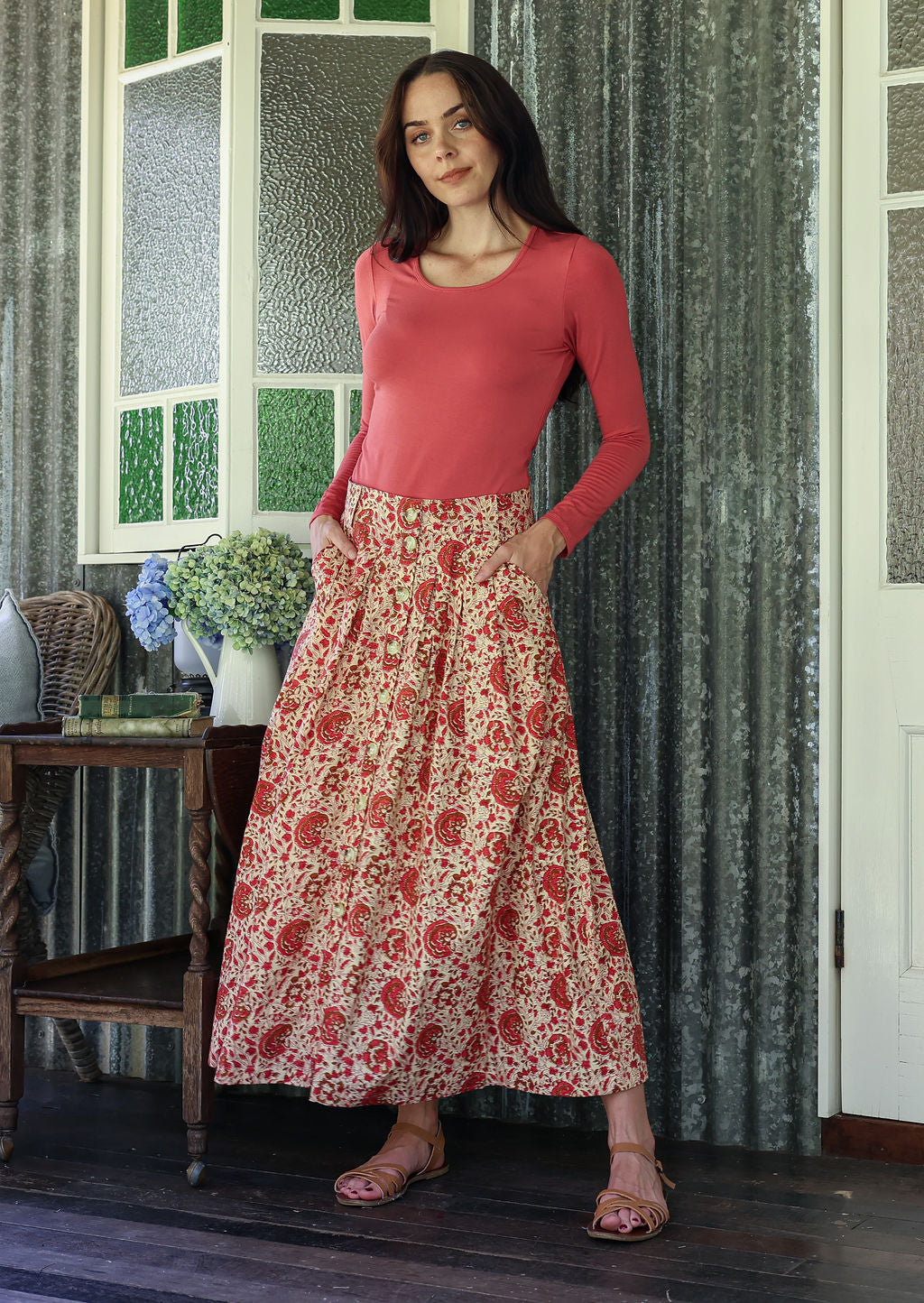 Woman standing with both hand in pockets wears 100% cotton button through skirt in gentle cream based floral print.