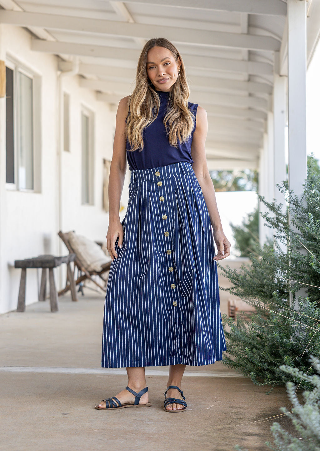 Woman wearing a navy basic top and button through shin length cotton skirt with box pleats, belt loops and pockets.