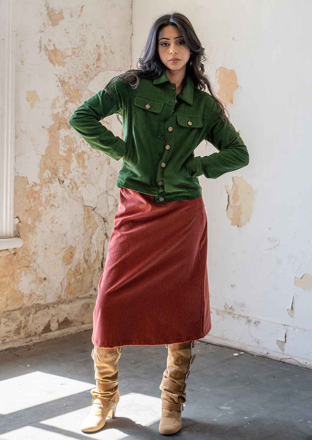 Woman standing wearing green brass button down corduroy jacket with hands in pockets