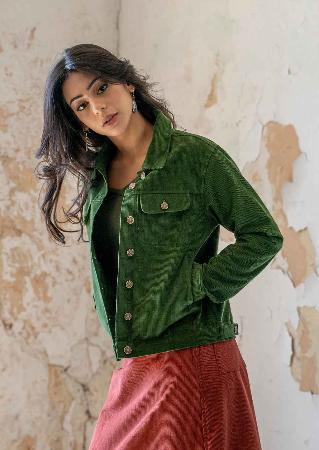 Woman wearing green brass button down corduroy jacket with hands in pockets