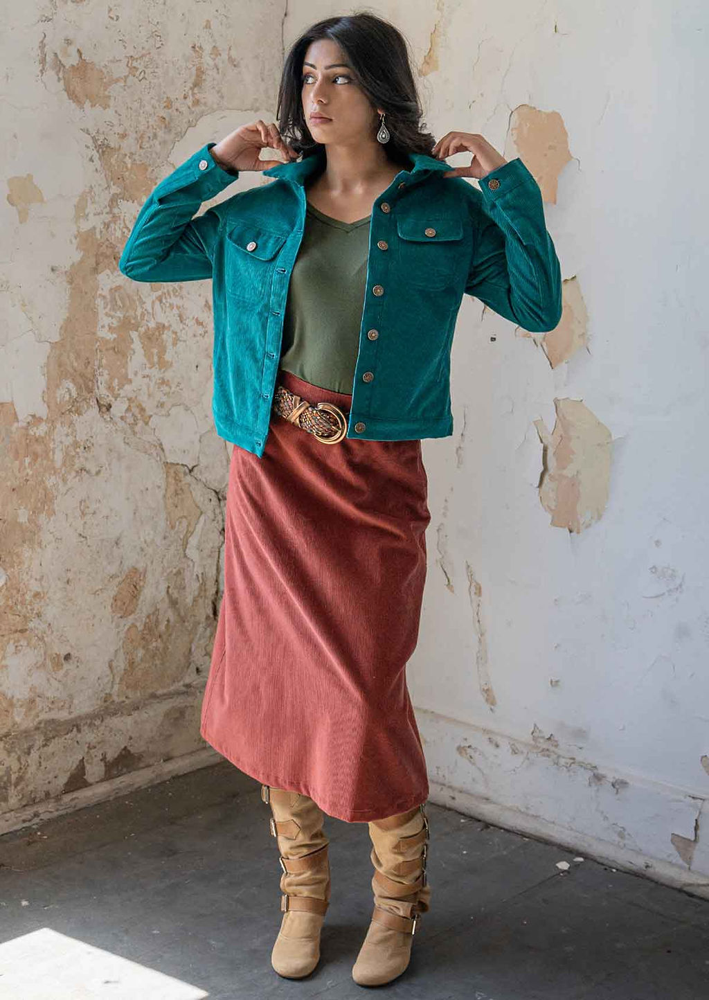 Woman standing wearing collared teal corduroy jacket with breast and front pockets, and brass buttons