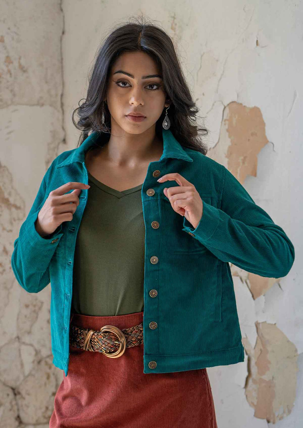 Woman wearing collared teal corduroy jacket with breast and front pockets, and brass buttons
