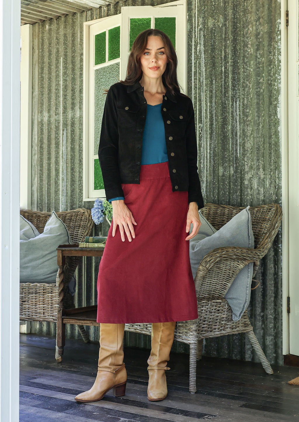 Woman in cotton corduroy red skirt and black jacket standing in a room with wicker furniture.