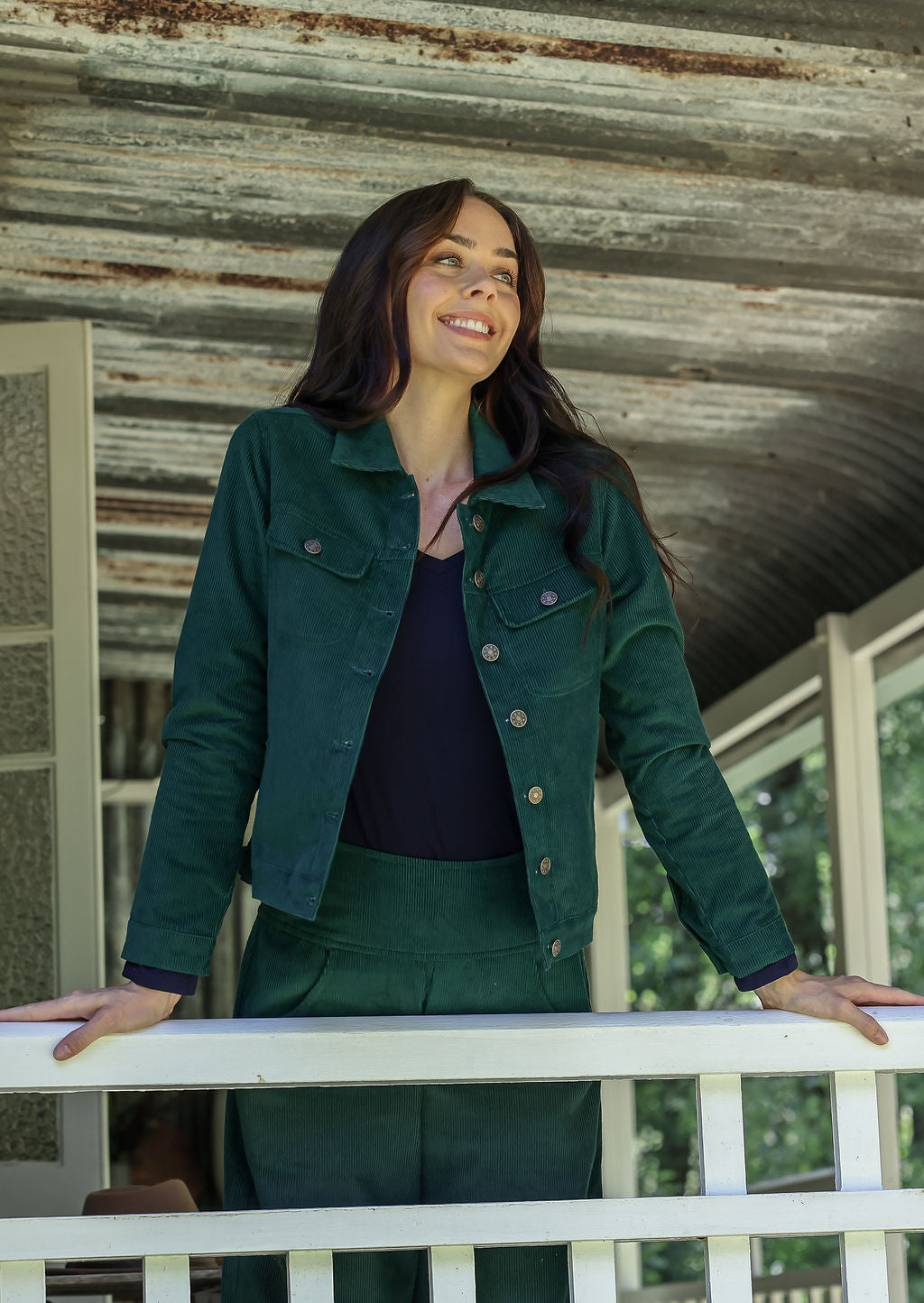 Woman in corduroy jacket standing on a porch with a rustic background