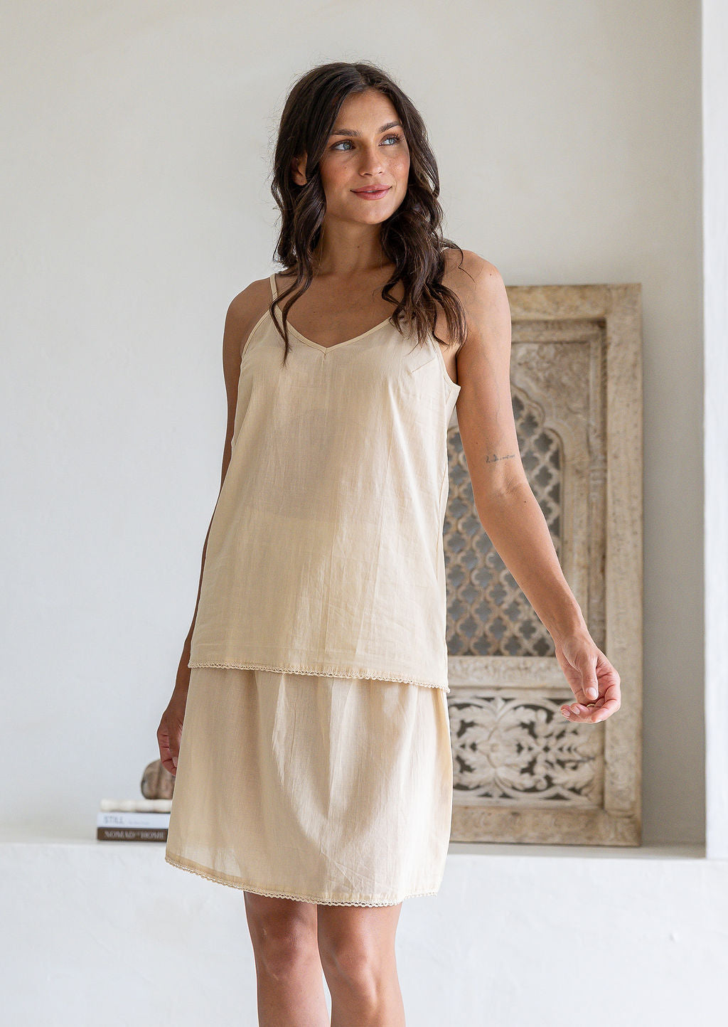 Woman poses in nude toned cotton voile above knee slip skirt with picot trim, paired with a matching cami