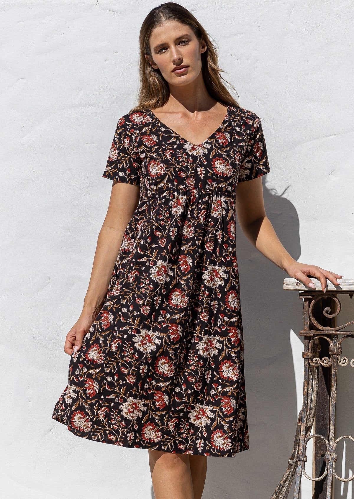 Model poses in a cotton V-neck short sleeve dress with empire waistline and pocket.