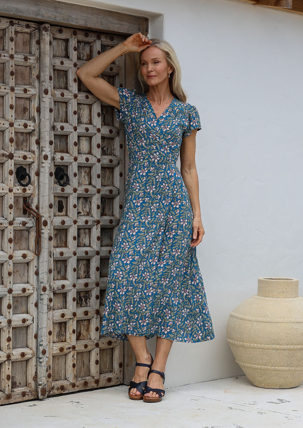 Woman wearing a 100% rayon, blue floral wrap around maxi dress with short cap sleeves and long fabric ties to secure the dress