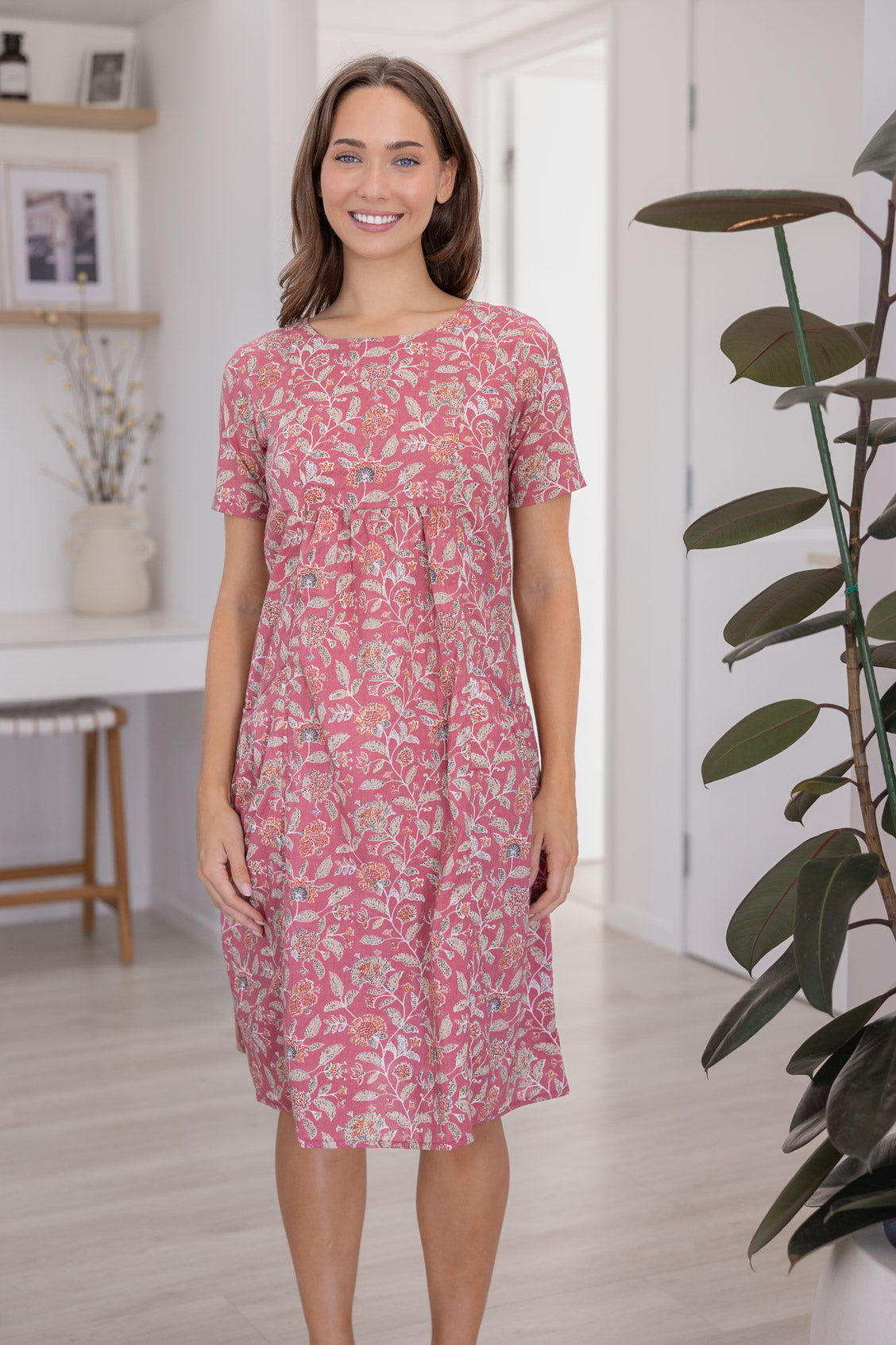 Woman wearing a 100% cotton dress with round neckline in warm pink based floral print.