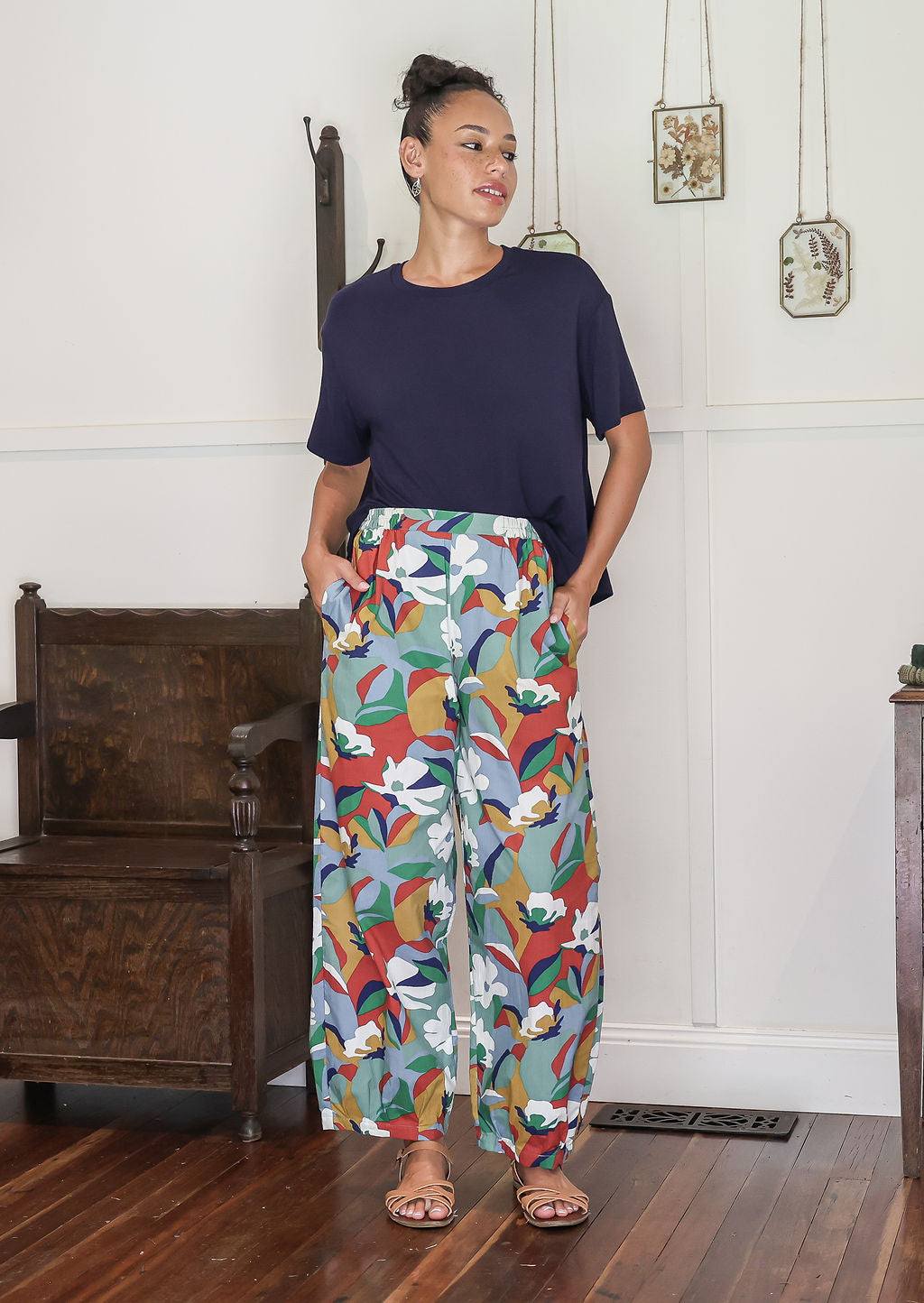Woman wearing a basic top and colourful floral cotton pants with hand in pockets standing in a decorative indoor setting.