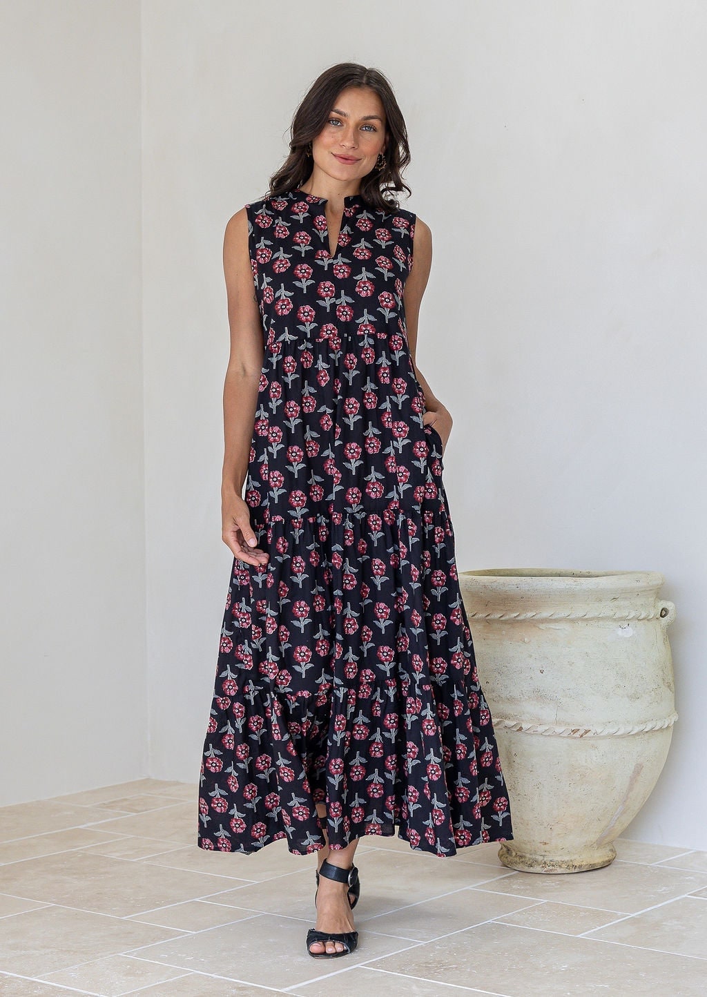 Woman poses in a cotton black floral tiered maxi dress with notch neckline, sleeveless.
