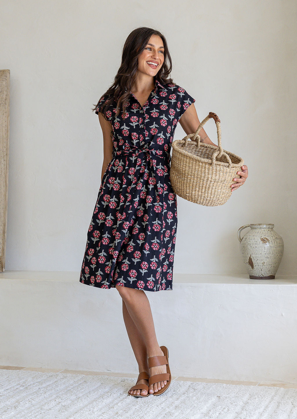Model stands wearing a 100% cotton knee length shirt style retro floral dress in black based floral print.
