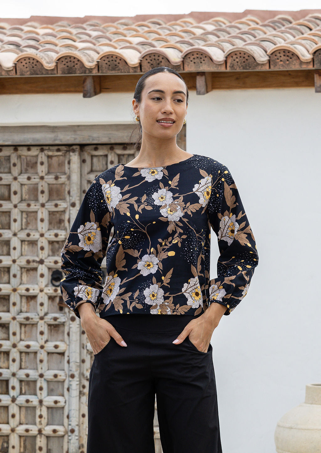 Woman wearing a dark floral cotton top with long bishop sleeves and boat neckline