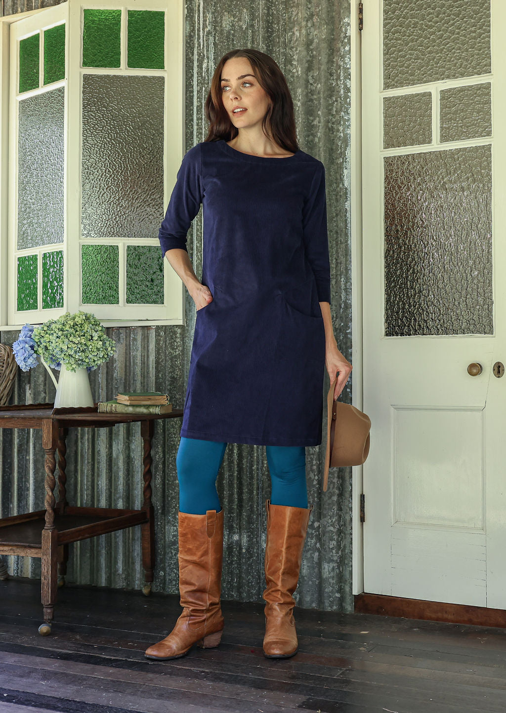Woman wearing green corduroy A-line tunic dress with 3/4 sleeves with one hand in pocket