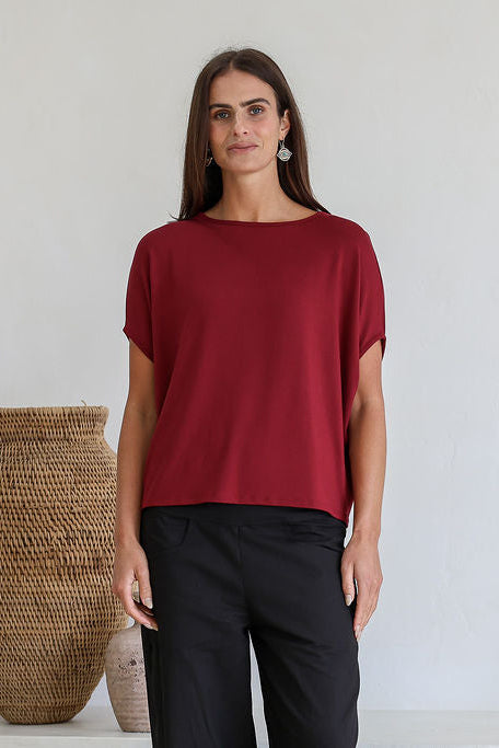 Woman wearing a maroon short sleeve batwing top with a round neckline, paired with black pants