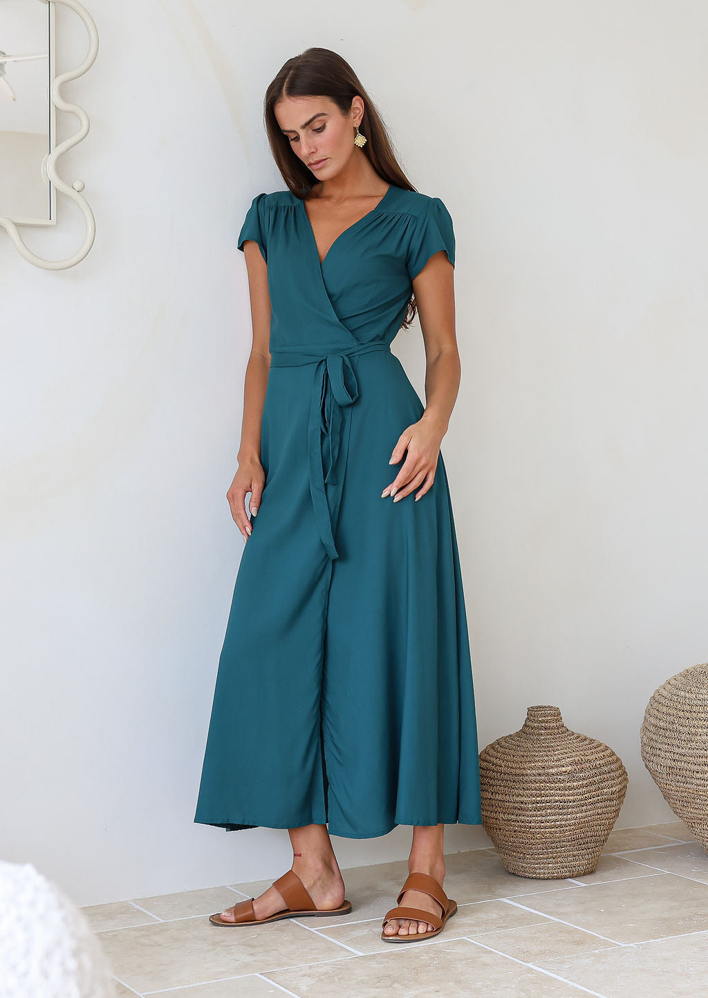 Woman leaning on a wall in a teal rayon wrap dress with gathers across front of shoulders